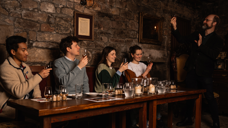 A Mercat Storyteller leading a group of 4 visitors through a whisky tasting in a candlelit underground cellar.