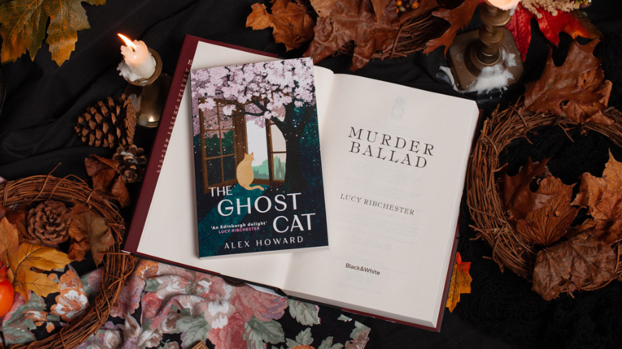 Murder Ballad by Lucy Ribchester and The Ghost Cat by Alex Howard, surrounded by autumnal decor like candles, brass decorations and autumn leaves and pinecones.