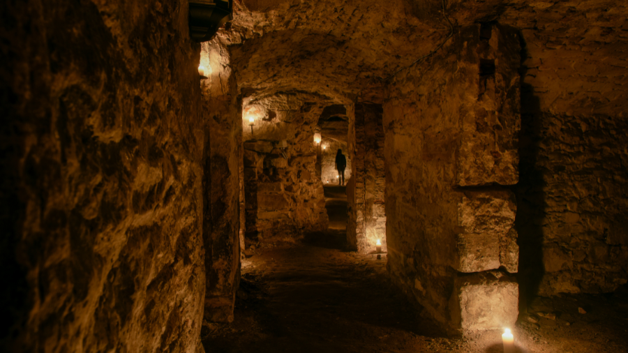 A corridor in the Edinburgh South Bridge Vaults leading into a room, the silhouette of a person standing at its far end. 