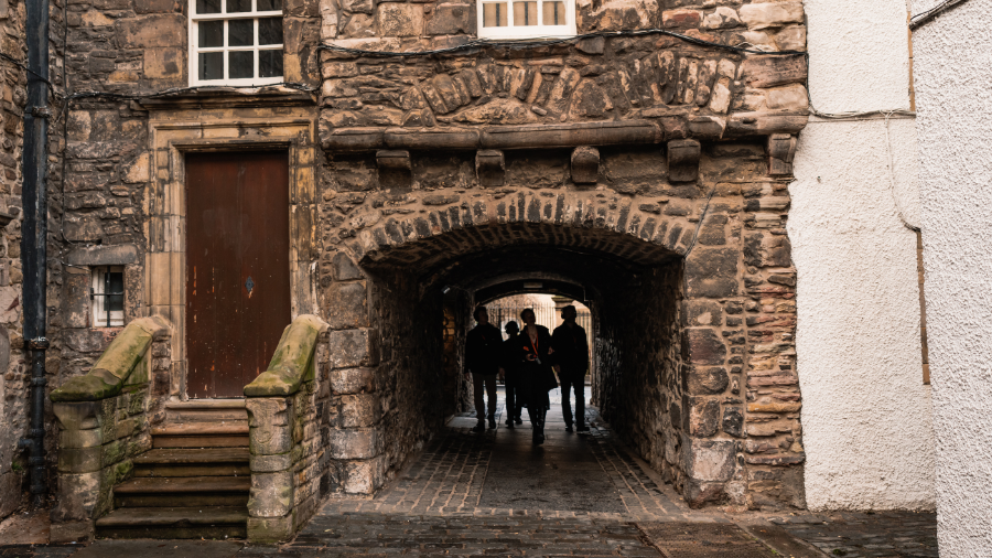 A Mercat Storyteller leading a group of visitors on an Edinburgh history tour, through the arched entrance to Bakehouse Close.