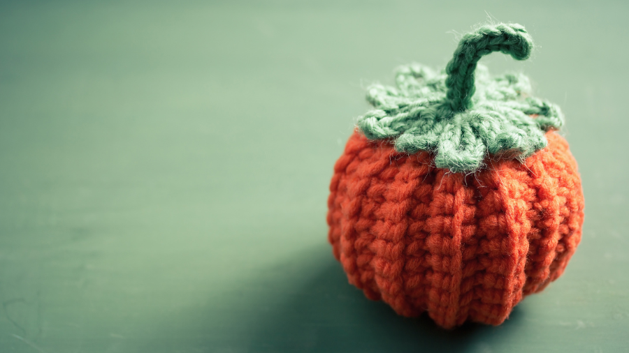 A small orange crocheted pumpkin on a green background. 