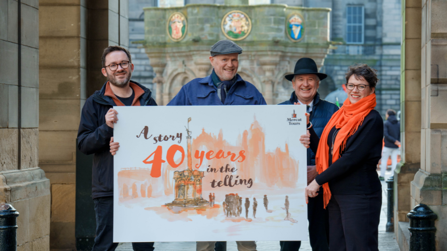 Mercat Directors and illustrator, Alastair, holding a sign showing a watercolour illustration of the Mercat Cross and St Giles Cathedral with script text reading 'A story 40 years in the telling' overlaid.