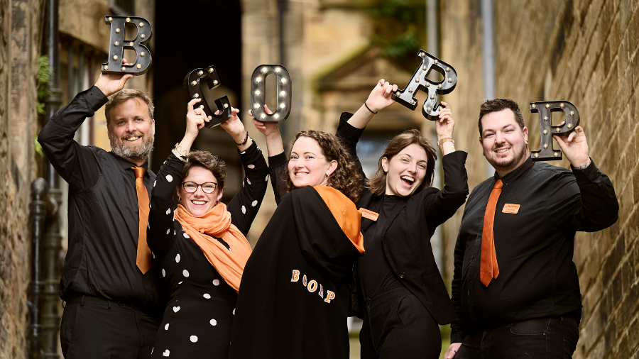 Members of the Mercat Tours team standing in an Edinburgh close, holding black letters that spell out B Corp.