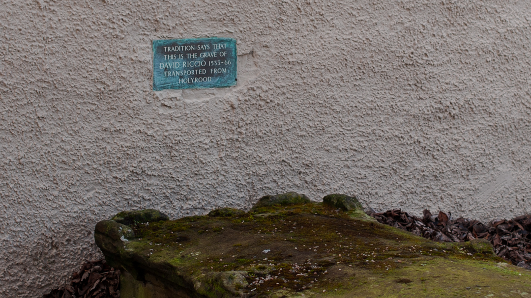 An oxidised plaque above a moss-covered grave reads ‘Tradition say that this is the grave of David Riccio 1533-66, transported from Holyrood.’  