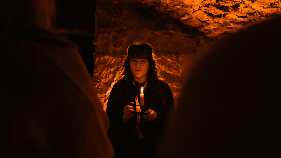 A Mercat Storyteller in a black cloak telling stories by candlelight in underground Edinburgh, the Blair Street Underground Vaults.